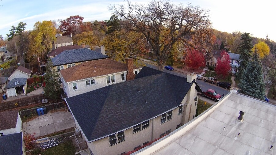 A dark replacement roof on a stucco home in an autumn Twin Cities street.